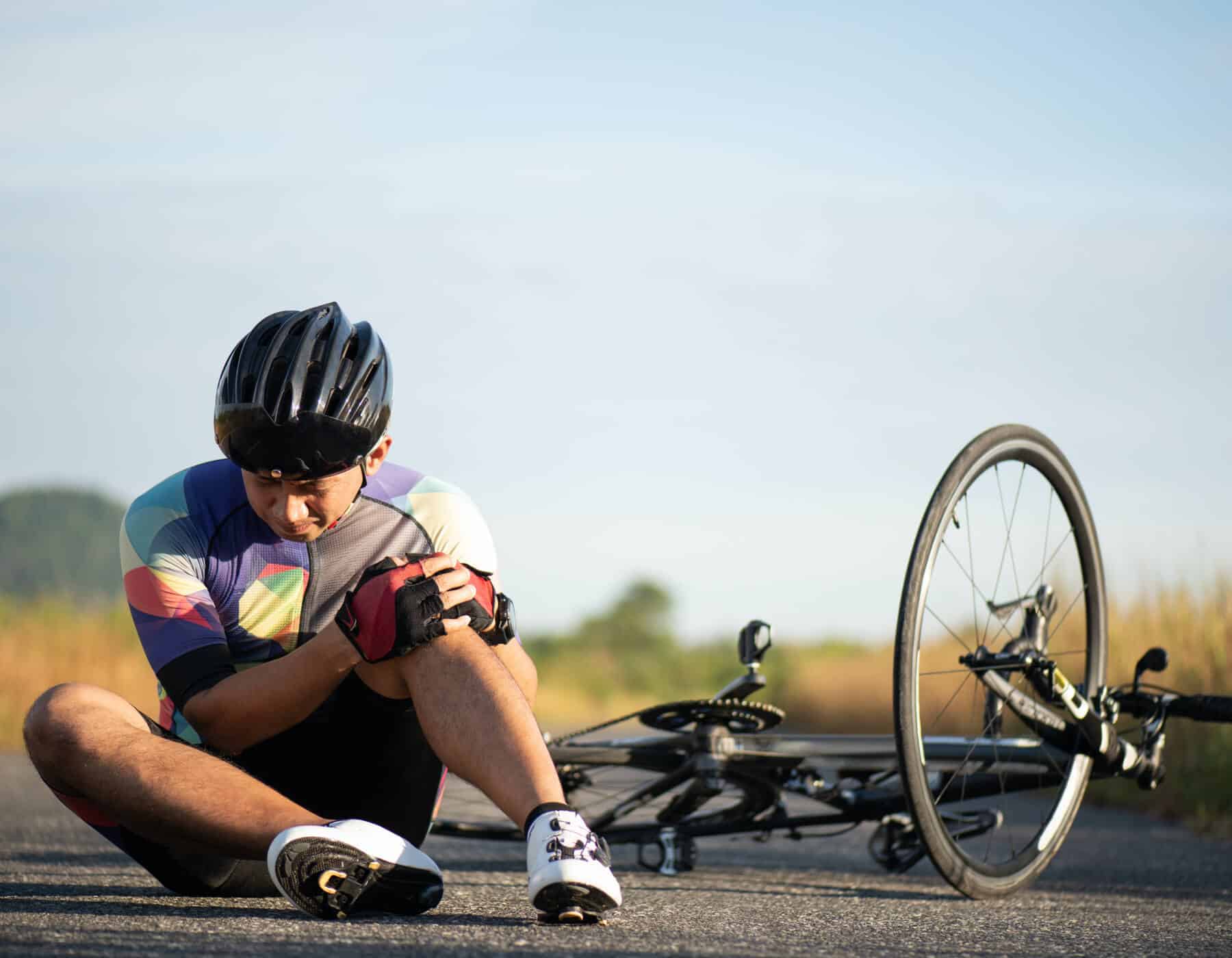 Bicycle accident person sitting on ground with helmet holding knee