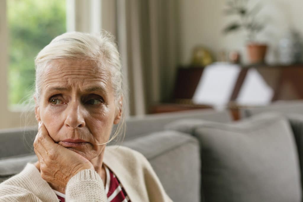 Front view of tensed active senior Caucasian woman with hand on face sitting on sofa in a nursing home