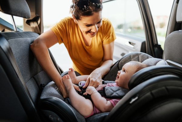 Mother putting baby girl in baby car seat