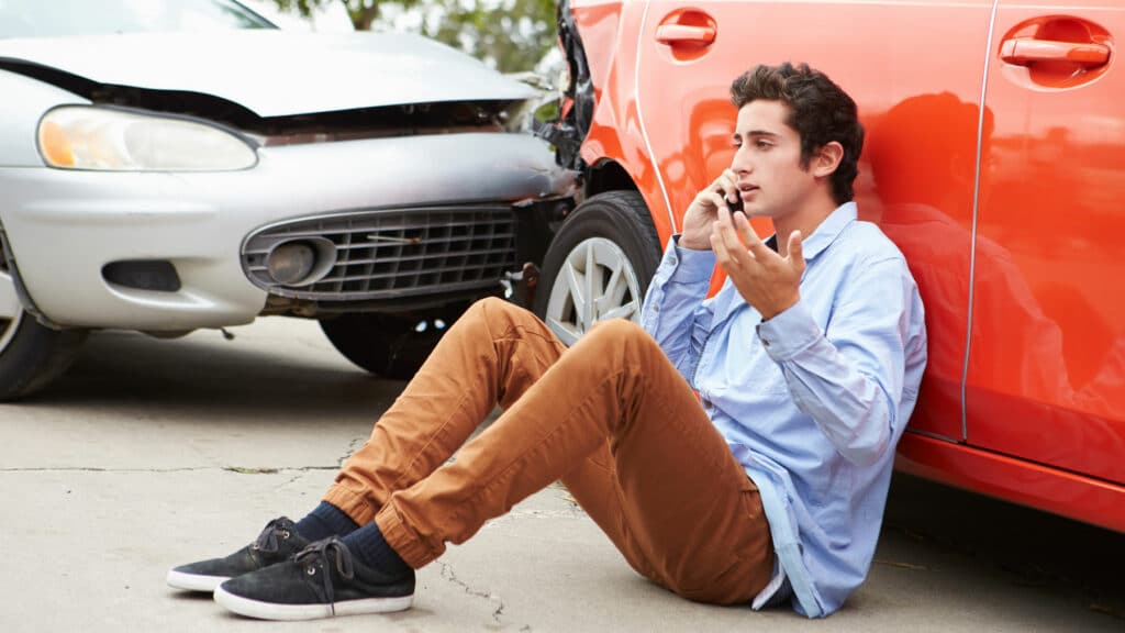 Person on phone sitting down in front of two cars in an accident