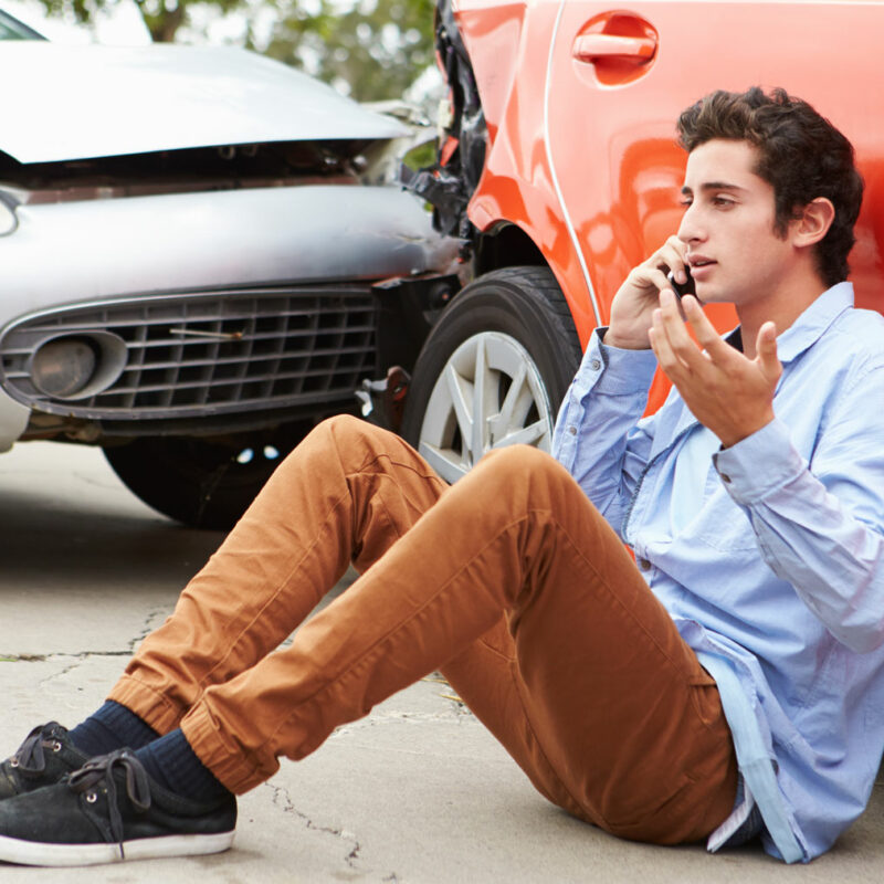 Person on phone sitting down in front of two cars in an accident